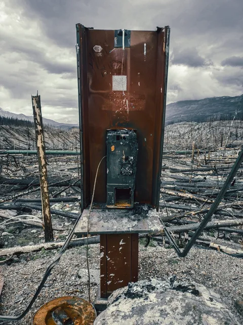 Restos de una estructura de servicios destruida por el incendio, con montañas al fondo.